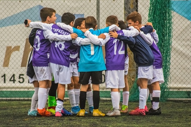 Youth soccer team in purple uniforms standing in supportive huddle with arms around teammates, representing teamwork and strategic collaboration for Q4 pipeline success