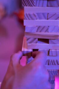 Close-up of hand carefully extracting wooden Jenga block from precarious tower showing business vulnerability from single partner dependence