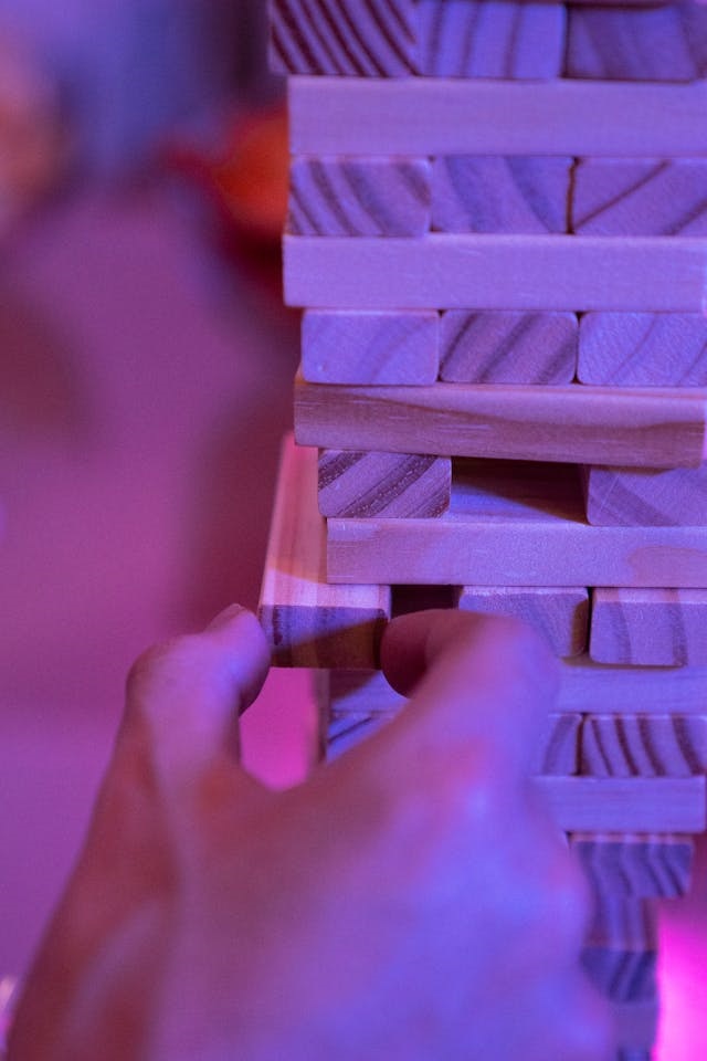 Close-up of hand carefully extracting wooden Jenga block from precarious tower showing business vulnerability from single partner dependence