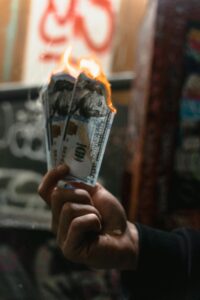 Hand holding burning hundred dollar bills representing the cost of investing in transactional referral partners instead of strategic referral partners